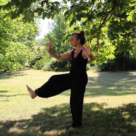 Woman wearing black does Tai Chi in a clearing in a park.