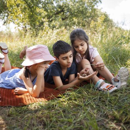 kids outside on a picnic blanket with books looking at grass and bugs
