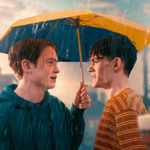 Charlie and Nick, from the Netflix series Heartstopper, look at eachother while standing in the rain.
