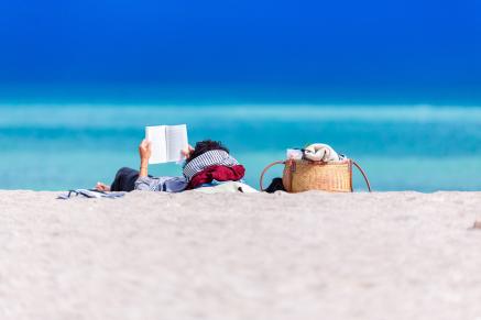 A person reads a book on a sunny beach.