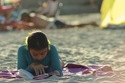 Young teen girl reading on a beach.