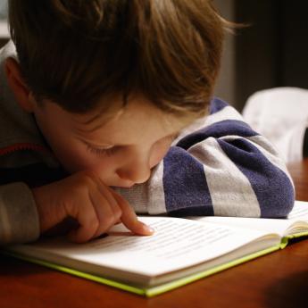 A young boy leans in close to a book while reading.