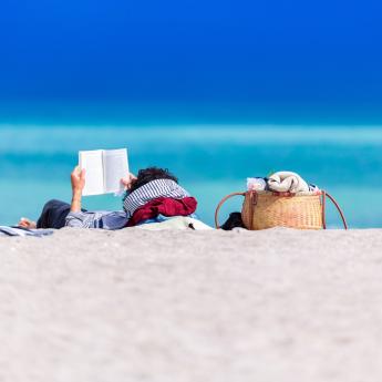 A person reads a book on a sunny beach.