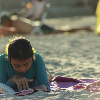 Young teen girl reading on a beach.