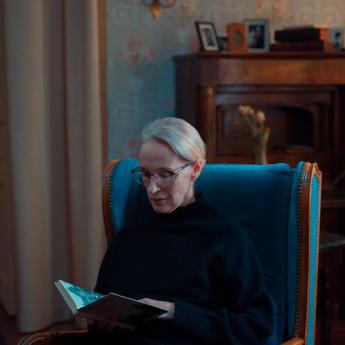 An older woman sits in a chair reading.