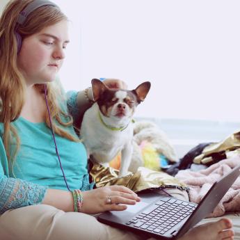 A teen girl with a dog sits reading a laptop.