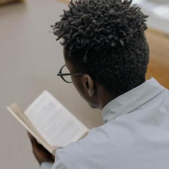 An over the shoulder shot of a Black man reading a book.
