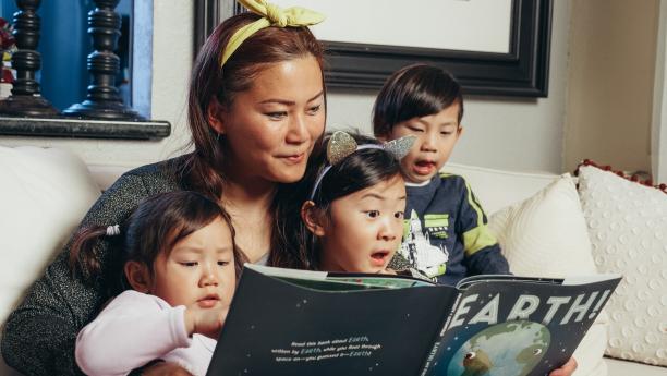 Image of Asian mother reading a picture book to three children