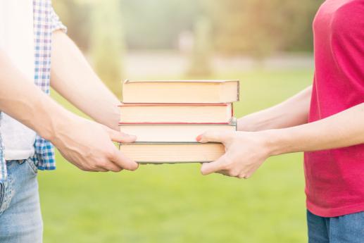 two people standing outside on grass passing books between eachother's hands