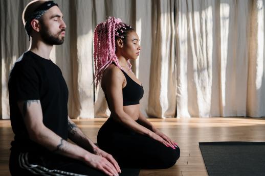 A male and female yoga students are sitting with their eyes closed in a studio.