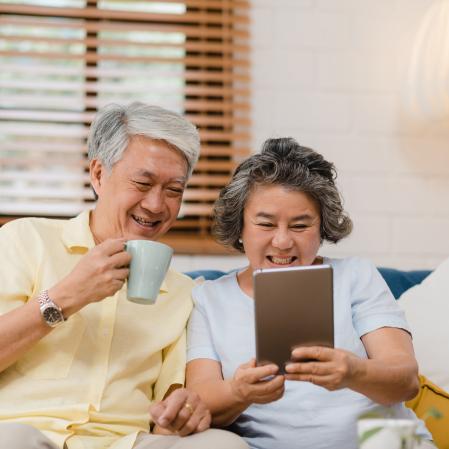 An elderly couple looks at a tablet while smiling.
