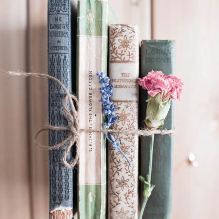 A bundle of books tied with twine with a pink carnation and lavender tied with it.