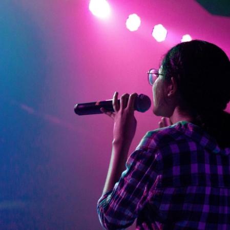 The back of a woman on a mic with pink and blue lights on a stage