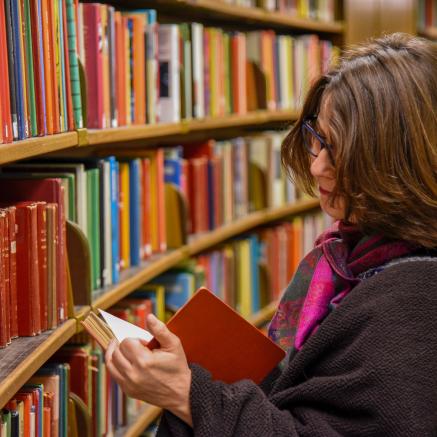 a woman looking at a book near a bookshelf