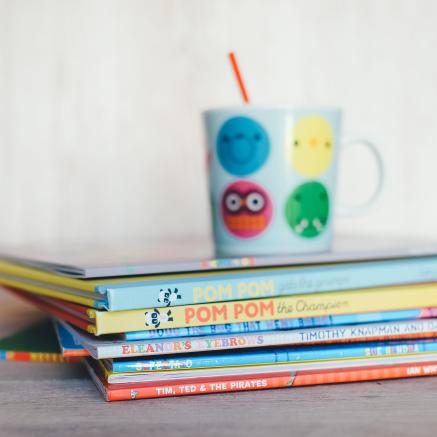 Children's books are stacked with a cup on top