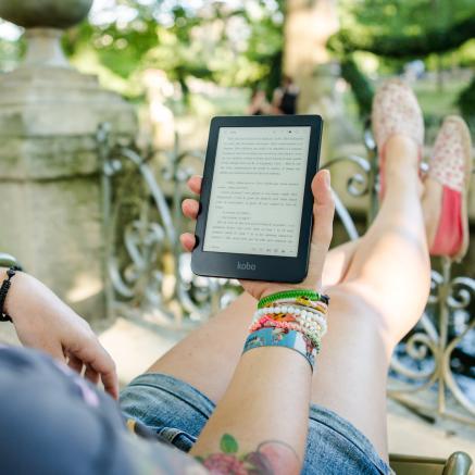 A person sits on their porch, reading an ebook on a Kindle device.
