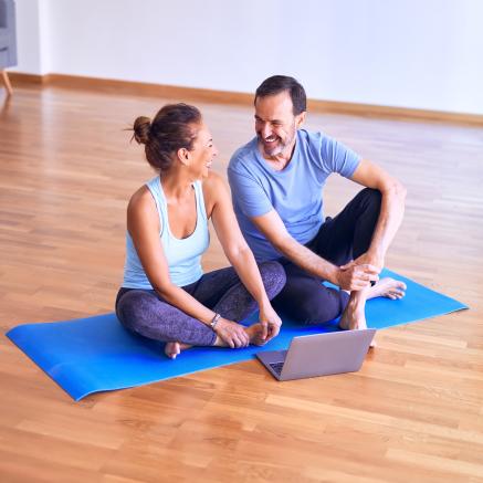 A couple sit together on a yoga mat before a class starts.