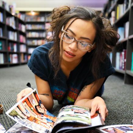 A teen sits on the floor, reading comics.