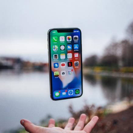 The photograph captures a mid air upward toss of an iPhone and the open hand that is ready to catch it. It's a nature scene in front of a river.