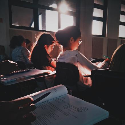 Students sit in a classroom with sunlight streaking throughthe window.