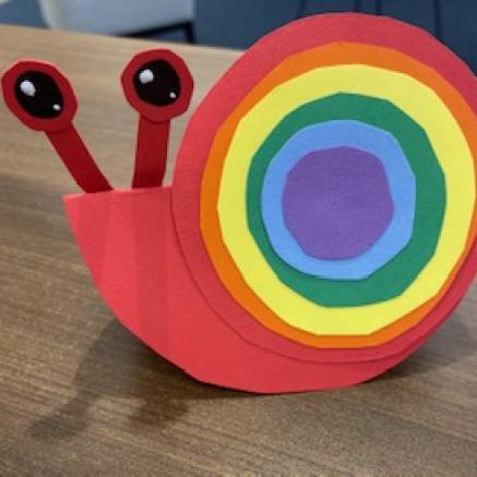 red paper snail craft with circular layered rainbow colored paper as its shell
