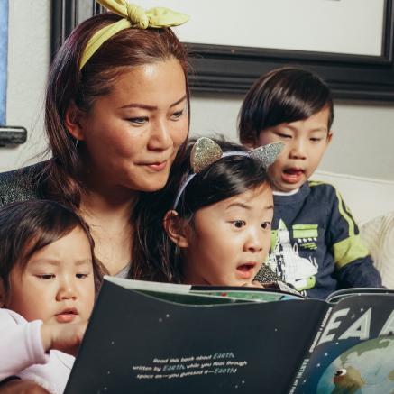 Image of Asian mother reading a picture book to three children