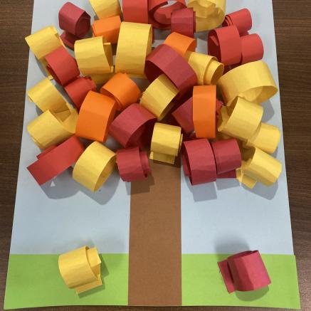 colorful rolled paper on top of a brown paper tree stump with a blue paper background -kids craft