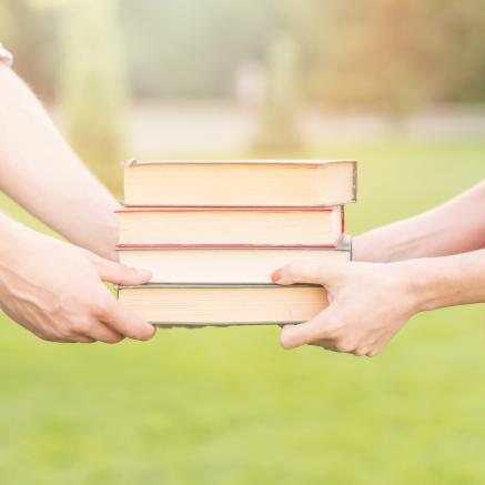 two people standing outside on grass passing books between eachother's hands