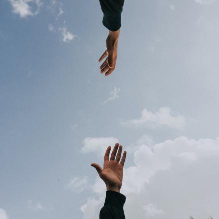 One arm and hand is reaching up towards another hand and arm reaching down.againsst the backdrop of a cloudy sky.