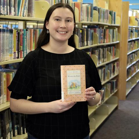 Cat, a BCLS staff member, holds up the book Winnie the Pooh by A. A. Milne