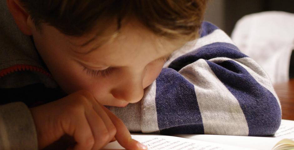 A young boy leans in close to a book while reading.