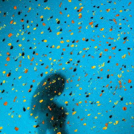 An abstract image of a person's silhouette against a blue background, many colorful specks appear across the image.