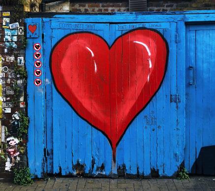 A red heart spray painted on a blue fence.