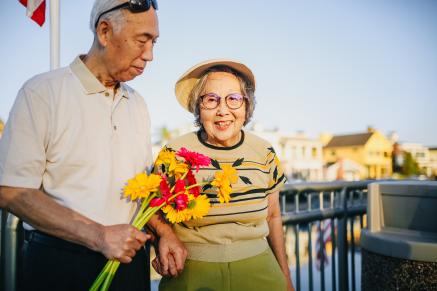 An Asian man holds flowers while an Asian woman looks at the camera.