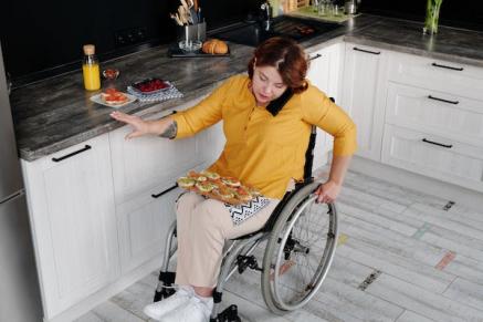 Woman in a wheelchair, wearing a yellow shirt and making dinner.