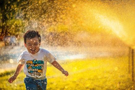 A child running through a sprinkler at sunset