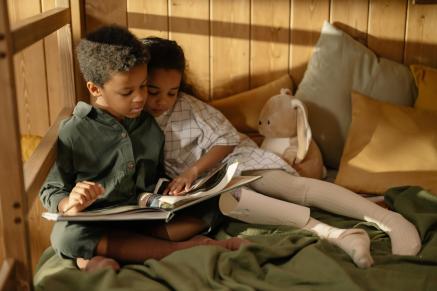 Two black children read a book together.