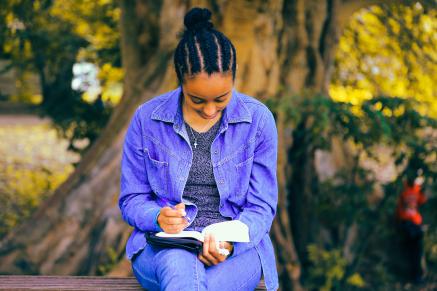 A Black woman with a purple shirt reads a book.