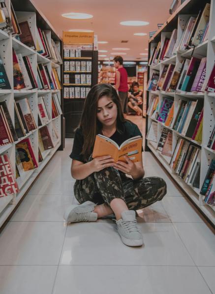 Teenage girl reads near library bookshelves.