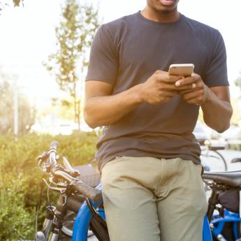 A man leans against his bike while looking at a smartphone