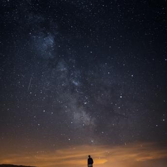 A figure stands looking up at the stars