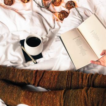 Coffee cup in bed with book and cozy socks