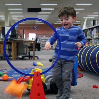 A young child throws a bean bag through a hoop during an event at the Evesham Library.