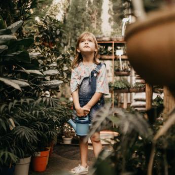 A young girl stands in a greenhouse, ready to water the plants