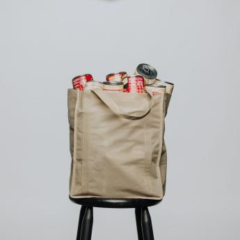 A reusable tote bag, filled with canned food, sits perched on a stool.