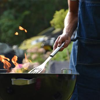 A person stands in front of a barbecue, cooking something.