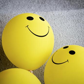 A pair of yellow balloons with smiley faces sit against a wall.