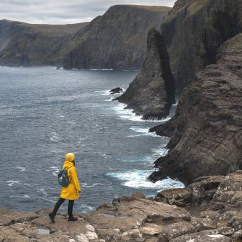 A woman in a raincoat walks along the cliffs