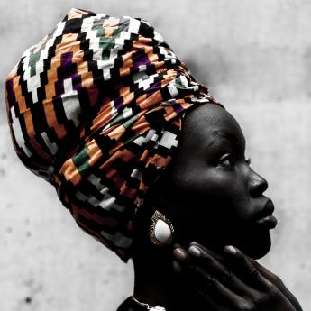 An African-American woman, wearing a headwrap, sits looking off into the future.