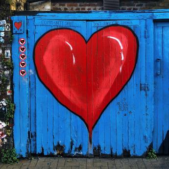 A red heart spray painted on a blue fence.